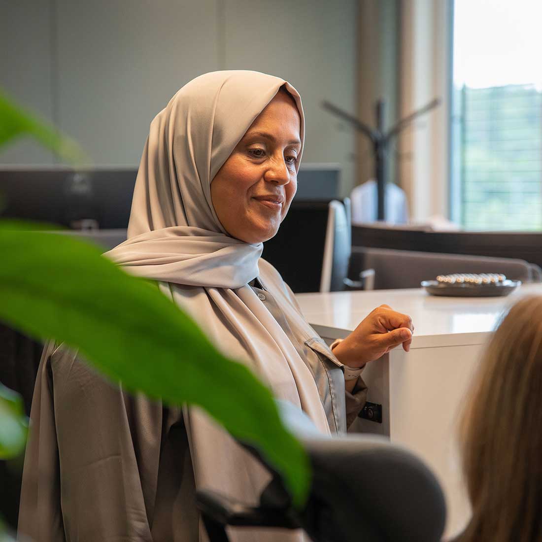 Muslim woman wearing a hijab in conversation with a colleague in an open office